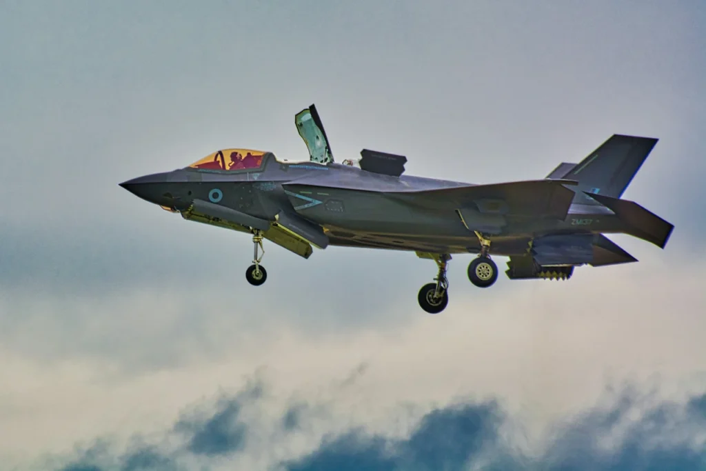 An F-35 aircraft in flight with its landing gear lowered and several aircraft doors open.