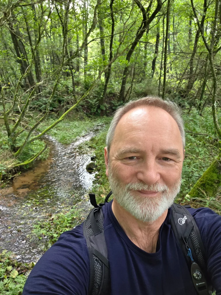 A walker beside a stream in green woodland.