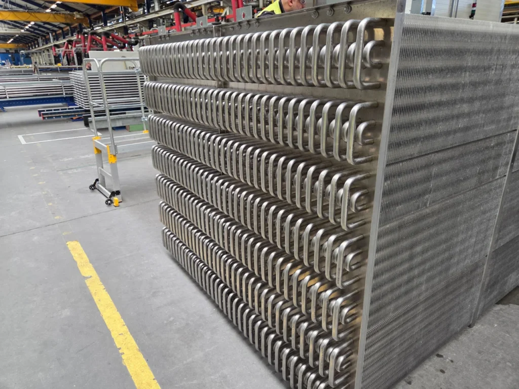 A large cooler assembly with rows of metal tubes and fins in a manufacturing hall.